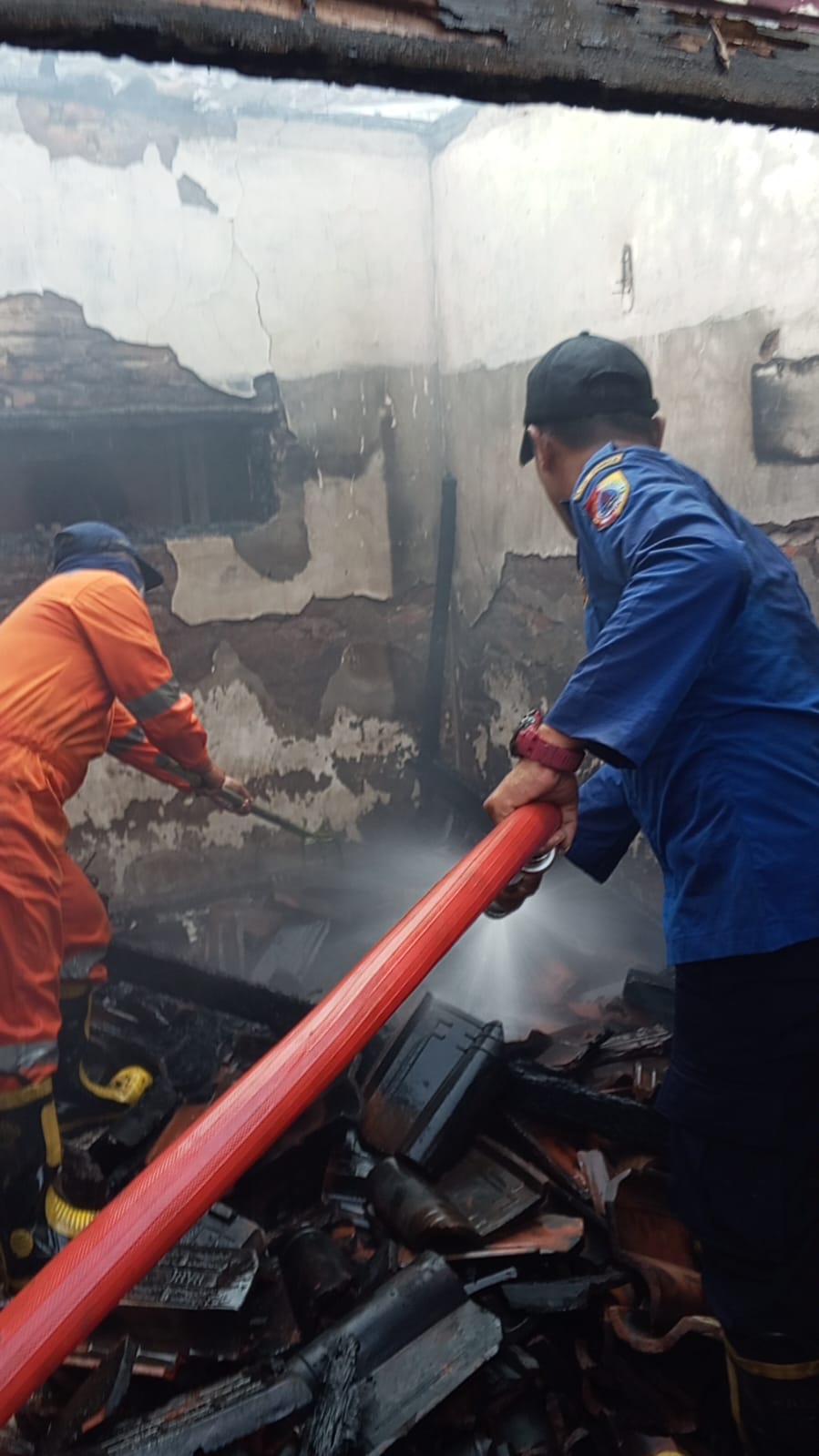 Petugas Damkar BPBD Jember melakukan pembasahan pada api yang membakar rumah korban. (Foto: Istimewa)